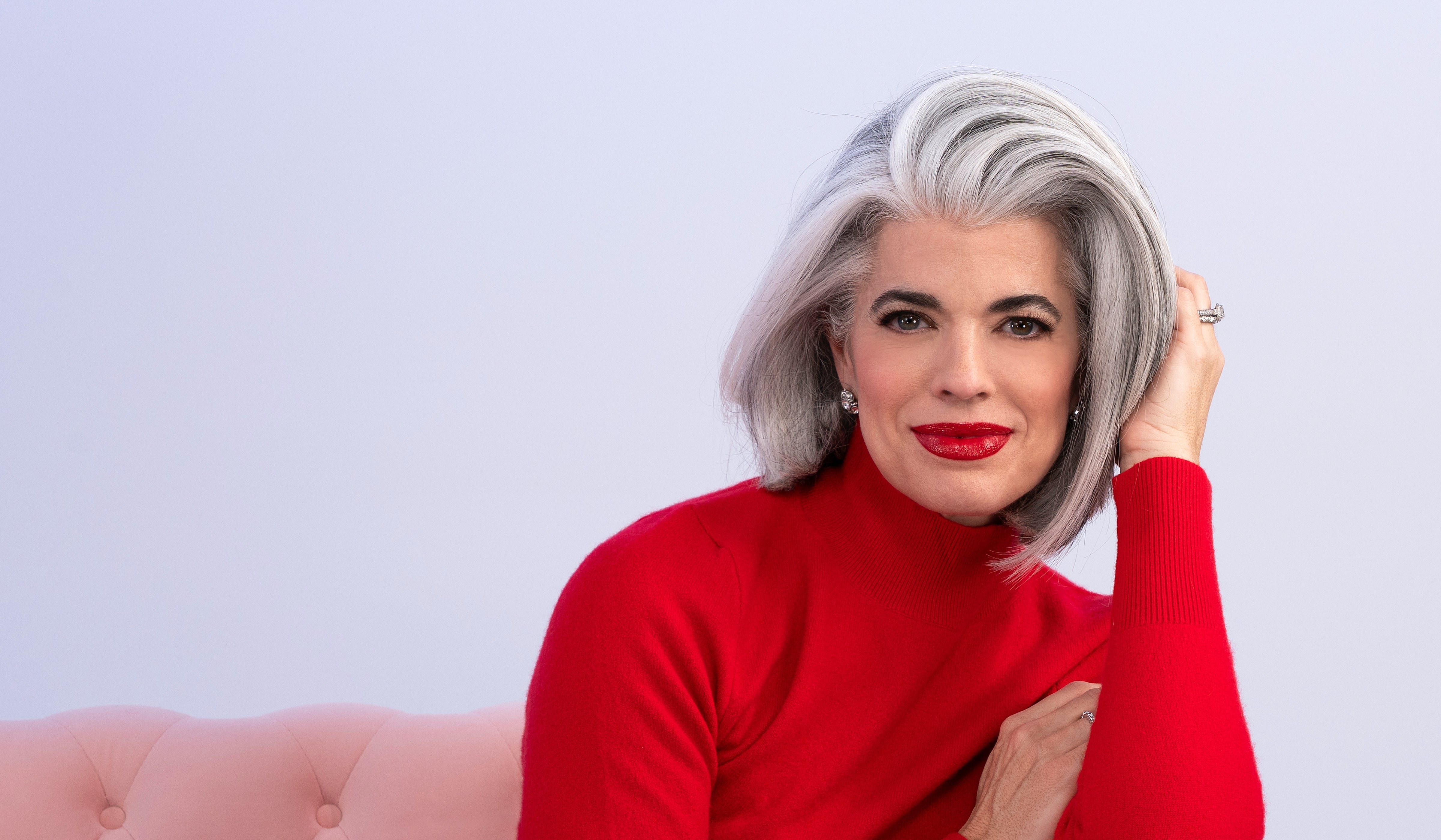 Person in red sweater sitting on pink couch, smiling confidently.