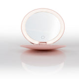 The Nikol Beauty 10x Magnification Mirror is a round, pink makeup mirror with a built-in LED ring light, shown open and standing upright on a reflective white surface.