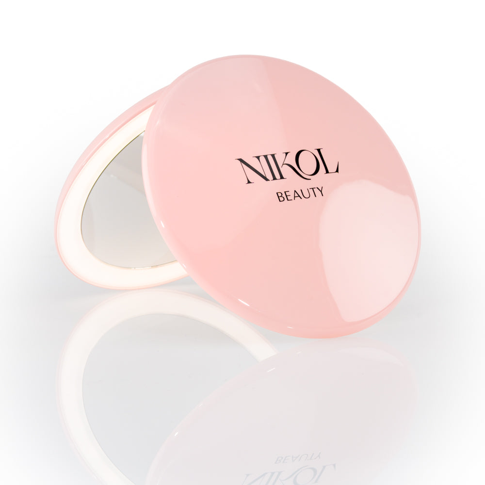 The Nikol Beauty 10x Magnification Mirror is a round, pink compact with the brand name on the lid, partially open to display its precise mirror, shown against a white background—perfect for detailed makeup touch-ups.