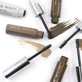 Nikol Beauty Brow Mascara tubes in various shades are open with wands displaying high-pigment browns. The wands lay on brush strokes of matching hues on a white background, promising defined eyebrows with each application.