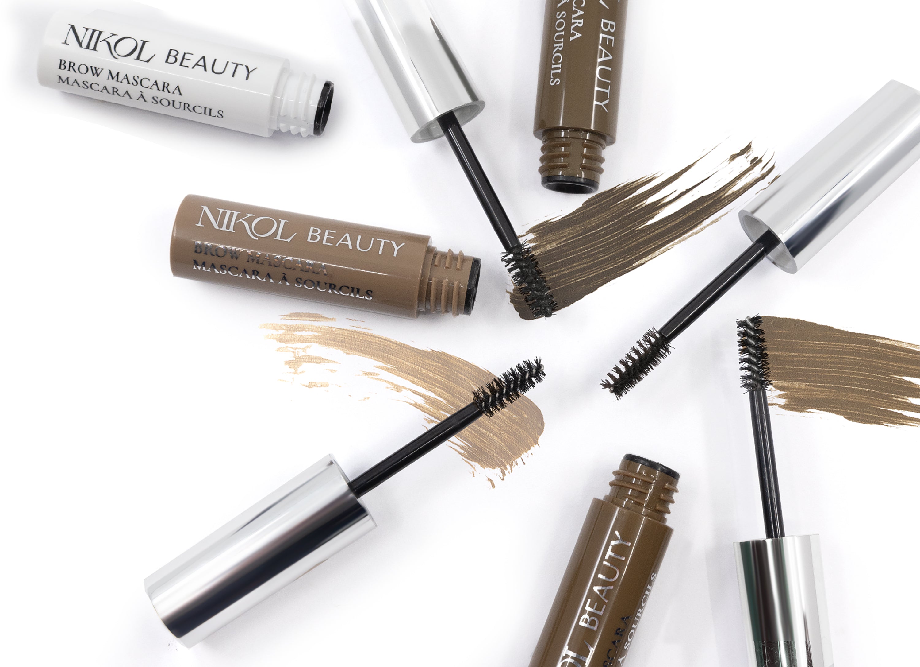 Nikol Beauty Brow Mascara tubes, with brushes out, display brown and beige swipes on a white background, ideal for defined eyebrows.