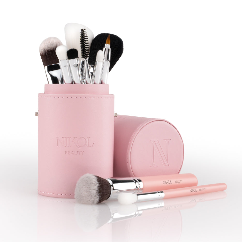 Introducing the Essential Makeup Brush Set by Nikol Beauty—a vegan travel set featuring pink-handled brushes in a matching cylindrical holder embossed with the Nikol Beauty logo. Three of the brushes are displayed in front, making this set ideal for beauty enthusiasts on the go.