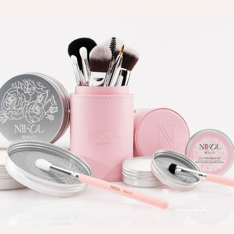 The Ultimate Brush Care Bundle by Nikol Beauty includes vegan brushes in a pink holder, tins of brush soap, and cleaning pads—a complete set for all your brush care needs.