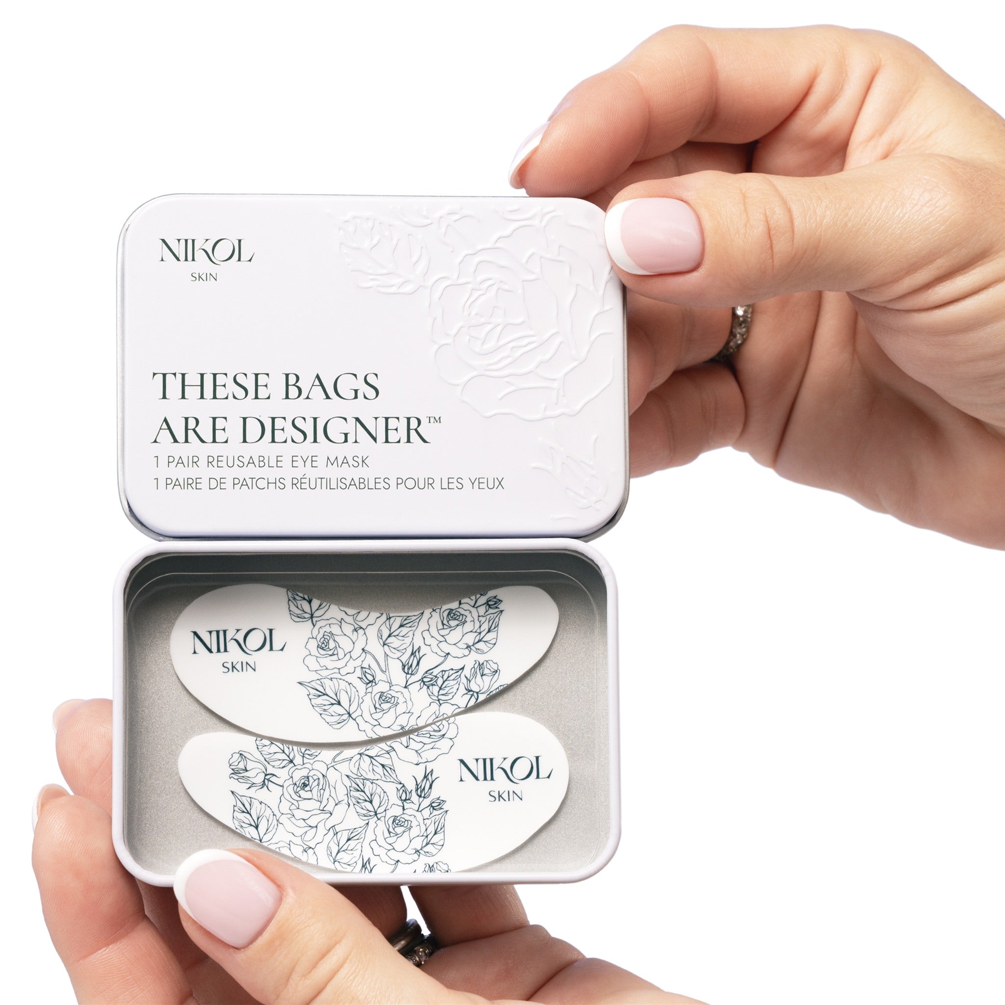 Hands opening the These Bags Are Designer tin to show the pair of floral silicone eye masks inside