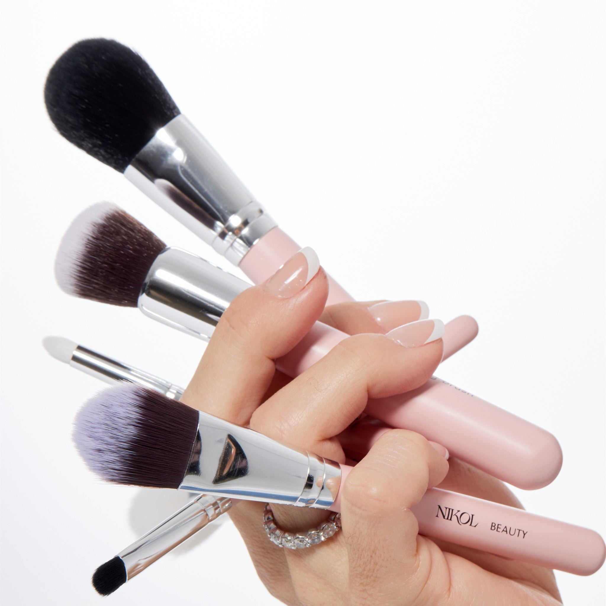 A manicured hand holding five pink-handled Nikol Beauty brushes fanned out