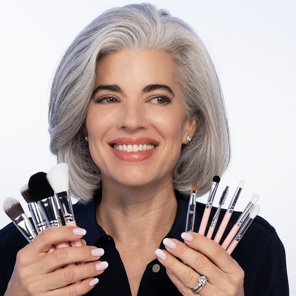 Nikol, with silver hair, smiling as she holds the Essential Makeup Brush Set fanned out in both hands