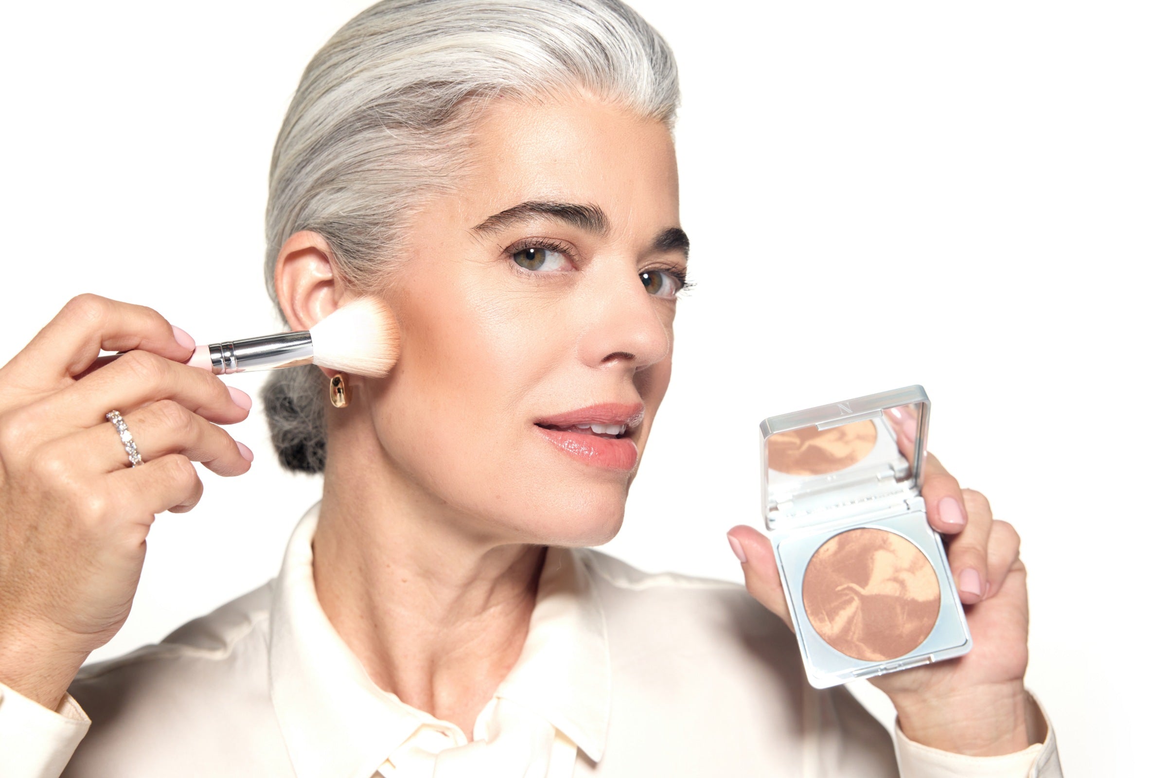 Nikol sweeping Crème Brûlée bronzer onto her cheekbone with a brush while holding the open compact