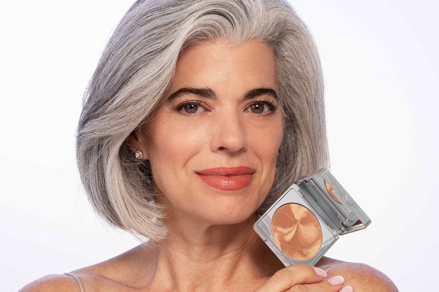 Nikol smiling and holding the open Crème Brûlée bronzer compact beside her face