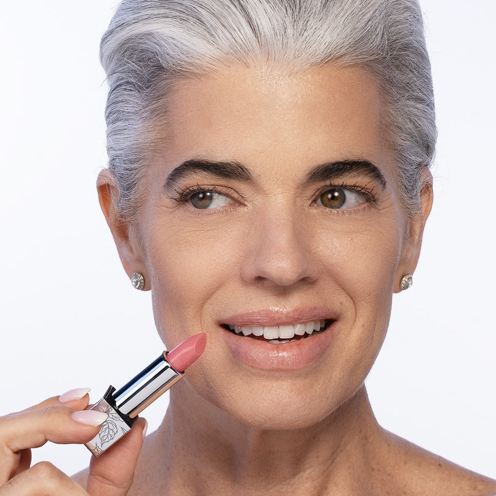 Nikol smiling as she holds the uncapped Rose Lip Balm up beside her lips