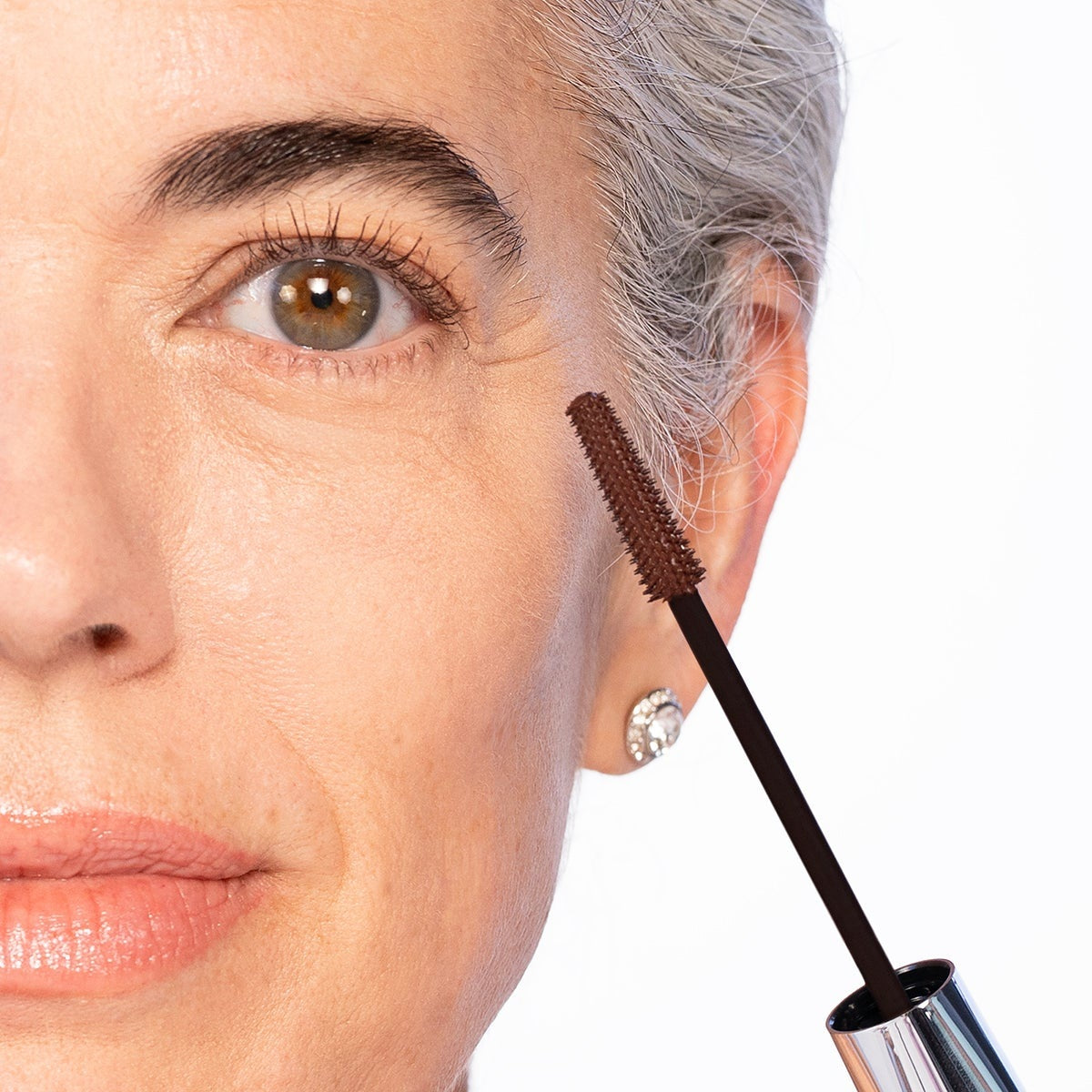 The Dark Brown VOLUME UP Mascara wand held beside a mature eye with full, defined lashes