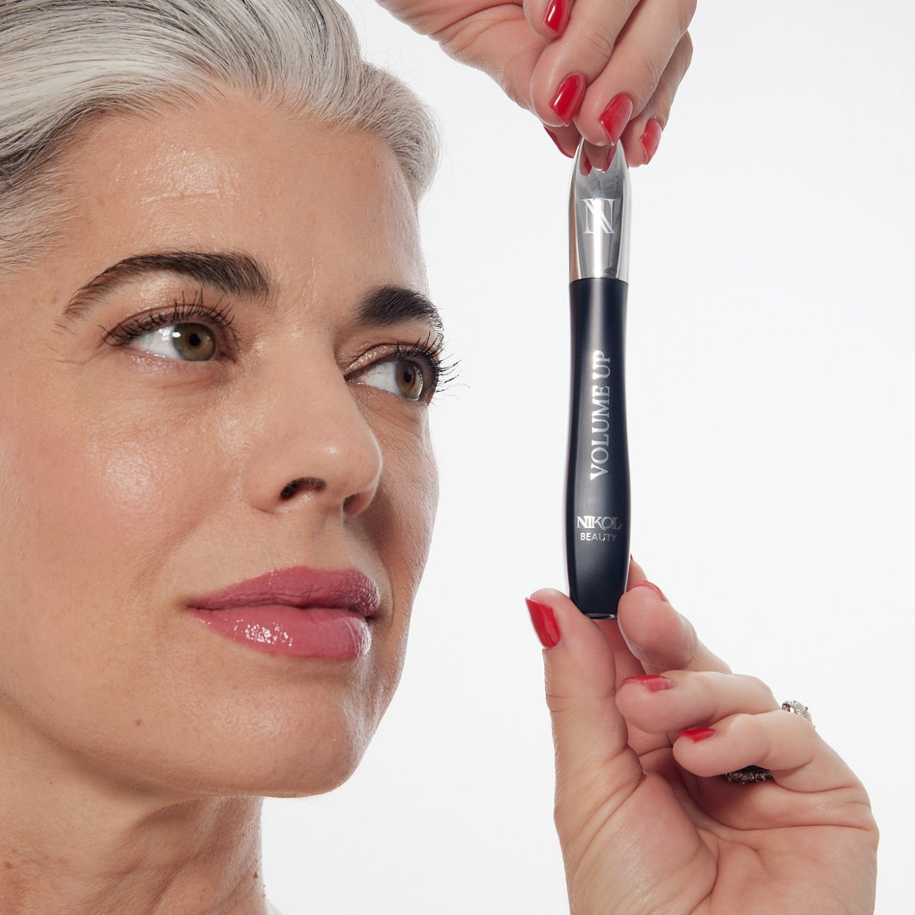 Nikol holding the VOLUME UP Mascara up beside her face, the wand drawn from the tube