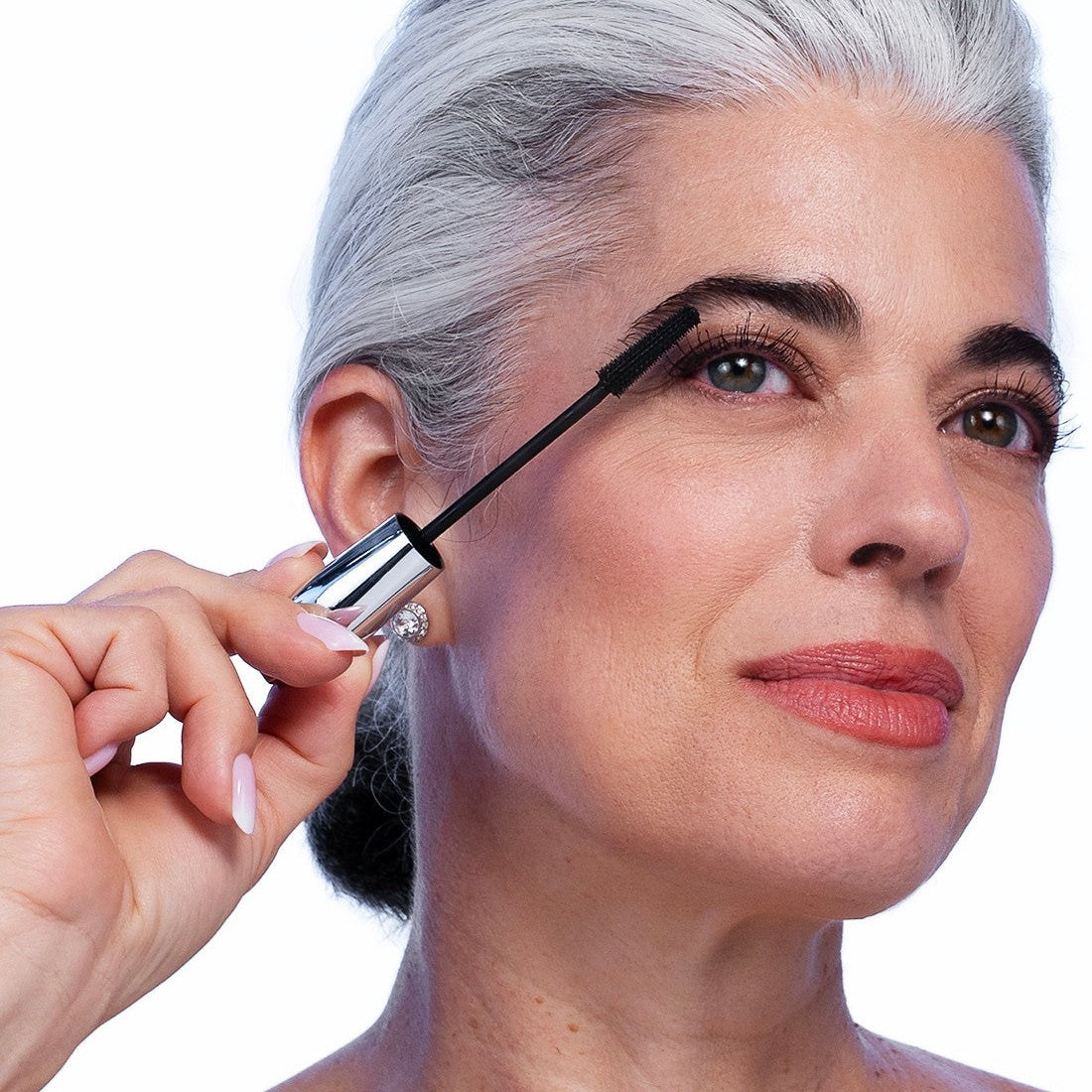 Woman with silver hair applying VOLUME UP Mascara to her upper lashes with the tiny-tooth wand