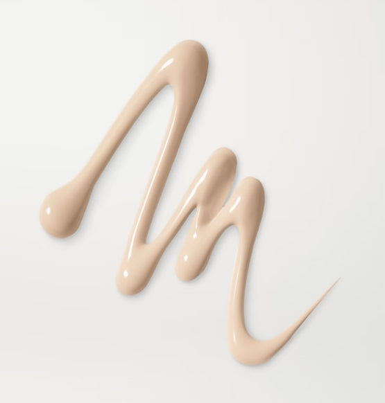 Smears of beige foundation form wavy lines on a white background. The smooth texture and slightly glossy finish suggest a creamy consistency.