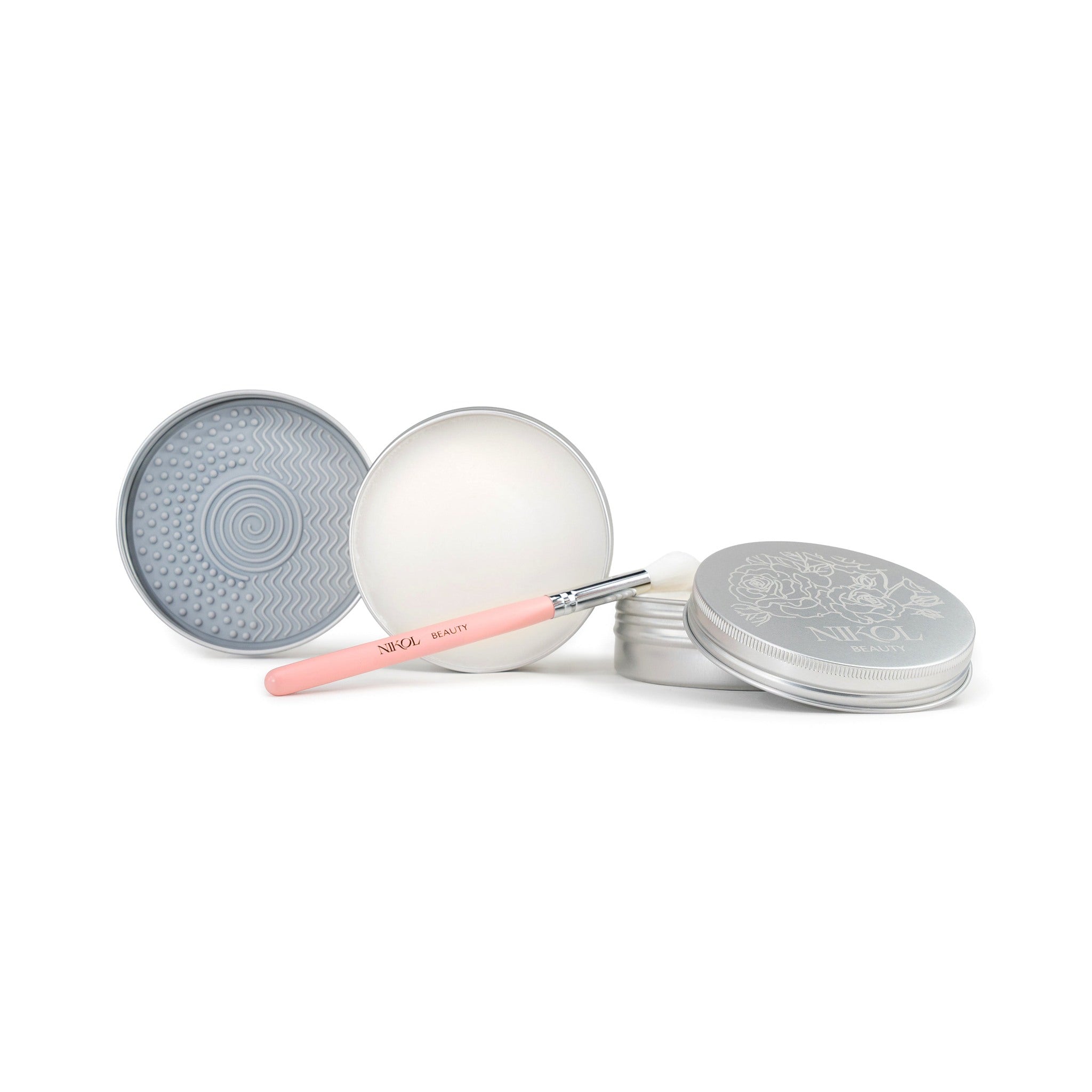 Three silver tins of Nikol Beauty Lux Brush Soap—one open to display the cleansing surface, one showing the soap, and a pink makeup brush with silver ferrule in front—an all-natural cleaner for effortlessly clean tools.