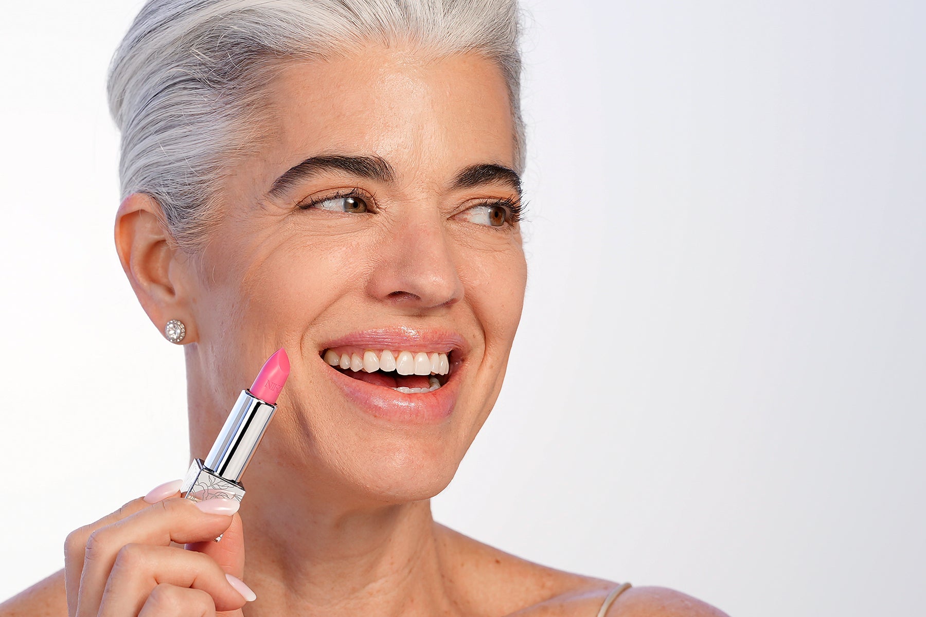 Nikol smiling as she applies the pink Rose Lip Balm