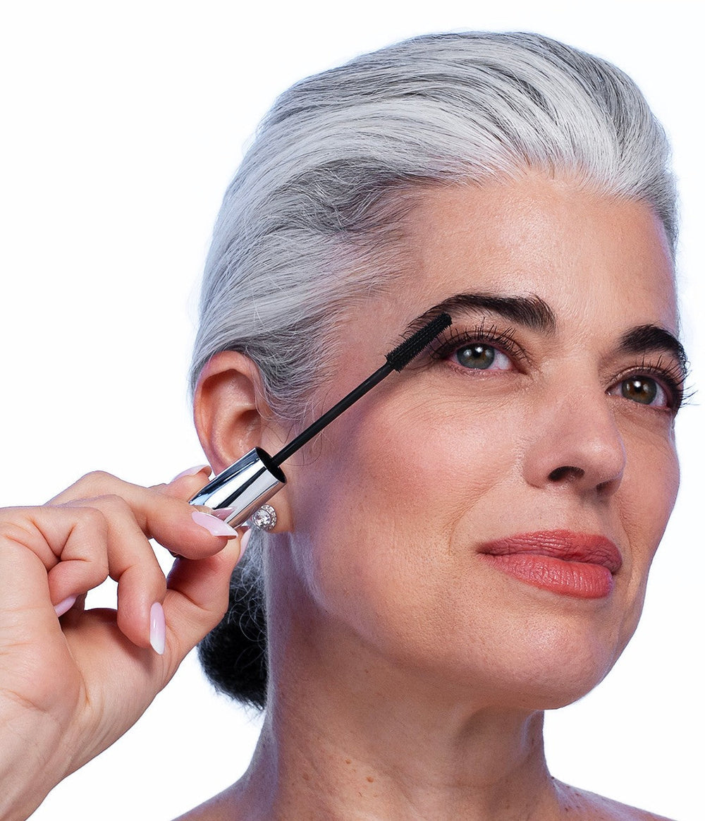 Woman with silver hair applying VOLUME UP Mascara to her upper lashes with the tiny-tooth wand