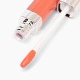 A close-up of the Defiance Lip Gloss #62 applicator from Nikol Beauty dipped in coral pink non-sticky gloss. The angled applicator is directed towards the viewer, with the tube seen in the background. This clean beauty product offers a shiny, smooth texture for high-impact shine.